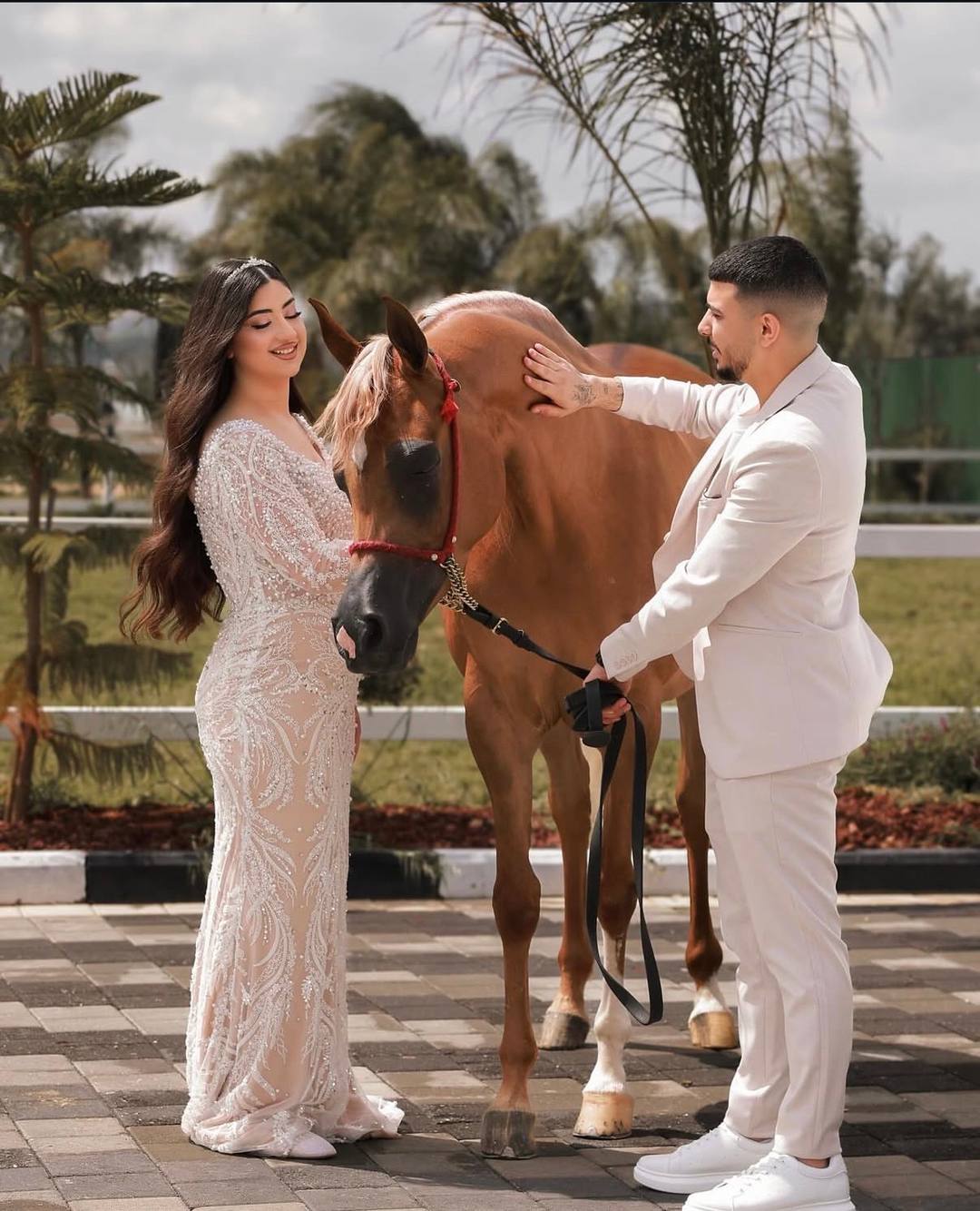 Bride and groom in a white suit beside a chestnut horse